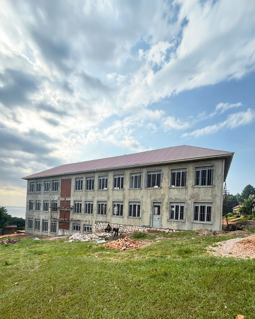 Blue cloudy skies sweep over the big new three story classroom block. Two builders are sitting beside the building taking a break.