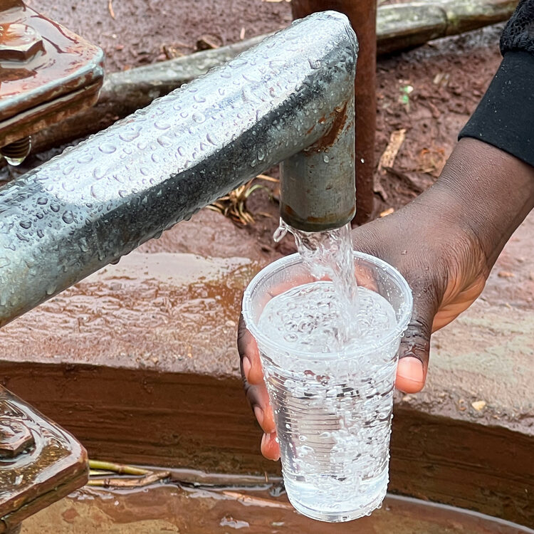 Clean water pours out of a borehole as someone fills a cup