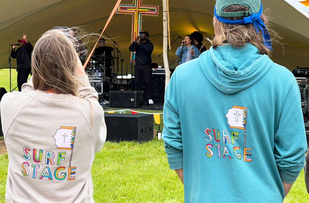 Two festival goers where different coloured surf stage tops as they watch the band play