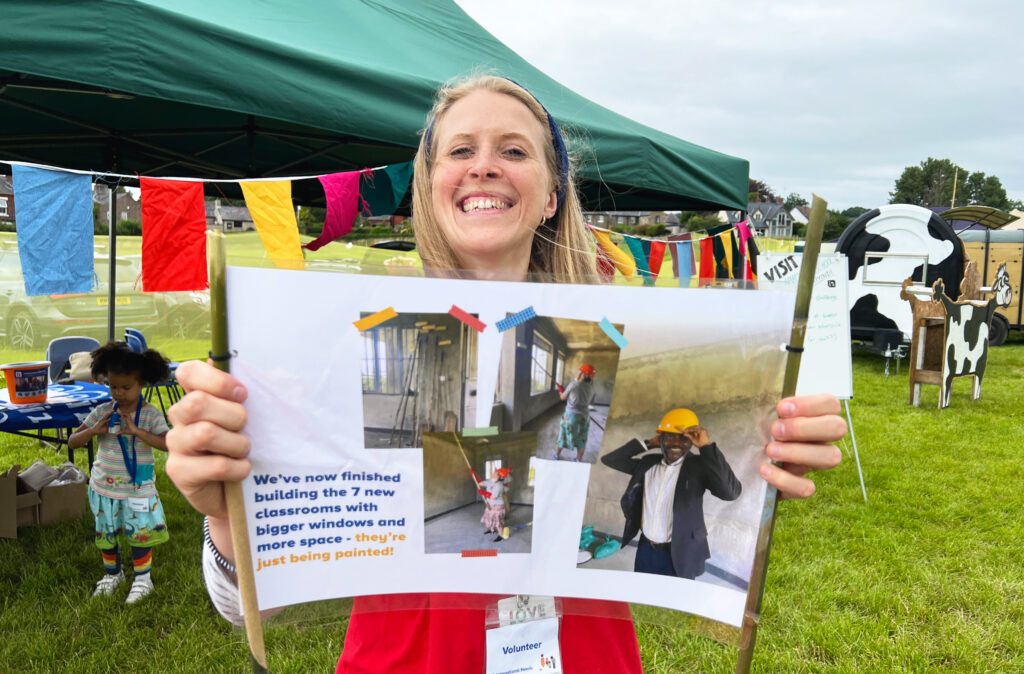 One of the International Needs team smiles holding a banner, with bunting in the backdrop