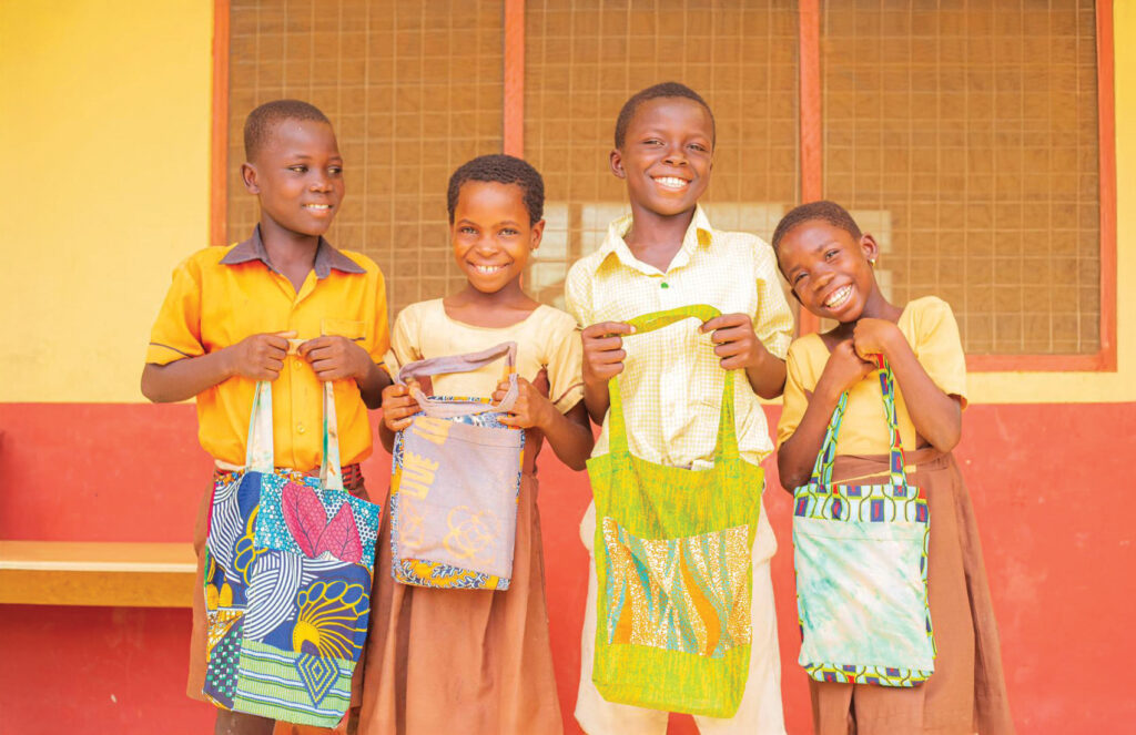 Four children smile cheekily and hold the handmade school bags 