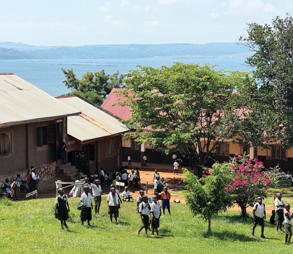 School huts beside a lake, with hills in the horizon, and students walking across a field