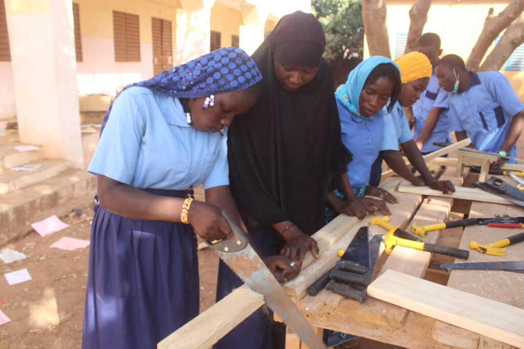 A girl is sawing wood with a couple of friends supporting the process